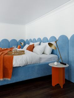 a bed with blue headboard and white sheets in a small room next to an orange side table