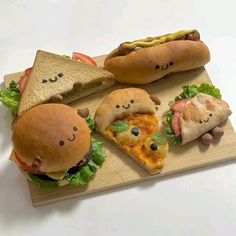 a wooden cutting board topped with sandwiches covered in toppings and face drawn on them