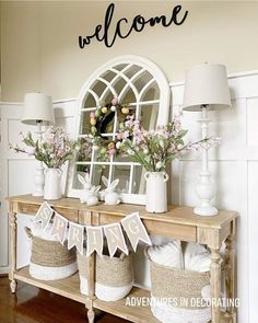 a wooden table topped with baskets filled with flowers next to a welcome sign on the wall