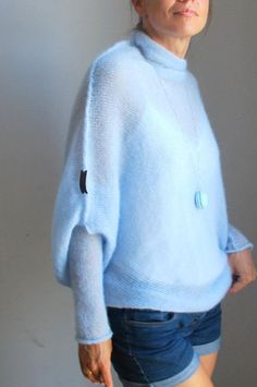 a woman wearing a blue sweater and denim shorts is posing for the camera with her hands in her pockets