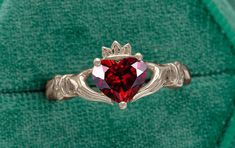 a ring with a heart shaped stone in the middle on a green velvet background,