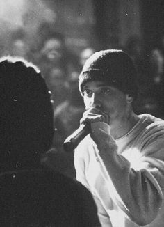 black and white photograph of a man holding a microphone in front of his face while standing next to a crowd