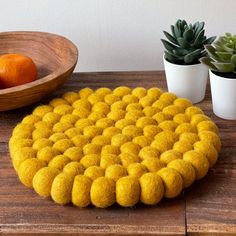 a wooden table topped with a yellow round rug next to a bowl of oranges