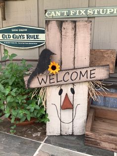 a wooden welcome sign with a scarecrow face and sunflower sitting on top of it