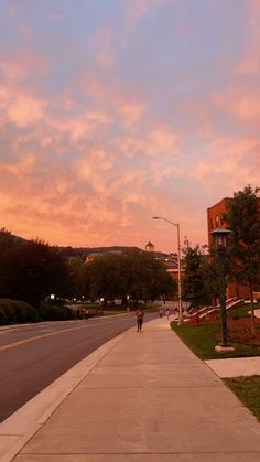 a person walking down the sidewalk in front of some buildings at sunset or dawn with pink clouds