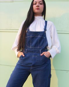 Vintage long dungarees in dark blue denim. Single front pocket. Front and back pockets. Size medium, UK 10-14 / EUR 38-42. Measurements - 9"(23cm) top of bib - 13"(33cm) bottom of bib - 32"(82cm) waist - 40"(102cm) hips - 27"(69cm) inner leg - 13.5"(35cm) rise. Material - Cotton & Modal mix. Condition - Excellent. Handpicked, repaired and ready to wear. This is an original vintage item, not new and minor signs of wear & age are expected, we will highlight any major flaws. Model is a UK 6/8 and is 5'7" tall. Dark Wash Utility Denim Jumpsuit With Bib Front, Utility Style Dark Wash Denim Jumpsuit With Bib Front, Denim Bib Front Overalls, Denim Bib Front Jeans For Workwear, Medium Wash Bib Front Overalls With Side Pockets, Utility Style Dark Wash Shortalls With Pockets, Utility Dark Wash Shortalls With Pockets, Utility Bib Front Bottoms In Dark Wash, Dark Wash Denim Shortalls With Pockets