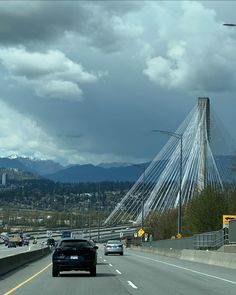 cars are driving on the highway with mountains in the background and cloudy skies above them