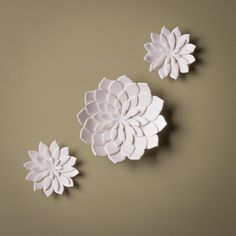 two white paper flowers sitting on top of a table next to each other in front of a brown wall