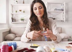 a woman sitting at a table working on some thread