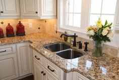 a kitchen with marble counter tops and white cabinets, flowers in a vase on the sink