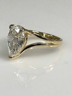 a yellow gold ring with a pear shaped diamond in the center, on a white surface