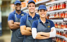 three workers are standing in front of the shelves with drinks on it and smiling at the camera