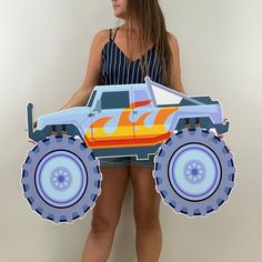 a woman holding a cardboard cutout of a monster truck with flames on the front