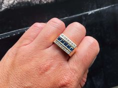 a person's hand with a ring that has three blue and white stones on it