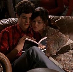 a man and woman are sitting on a couch reading a book while looking at each other