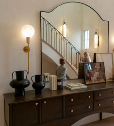 a dresser with a mirror, vases and pictures on it in front of a staircase