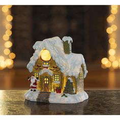 a small christmas house on a table with lights in the background