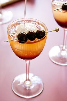 two martini glasses with olives in them on a table