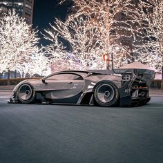 a futuristic car is parked on the street in front of some trees with christmas lights