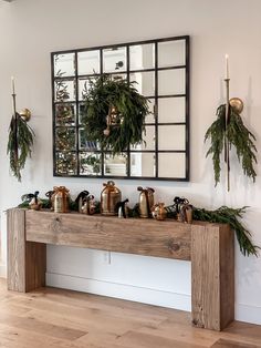 a wooden table topped with lots of greenery next to a mirror and candle holders