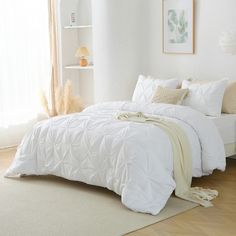 a bed with white comforter and pillows in a room next to a window,