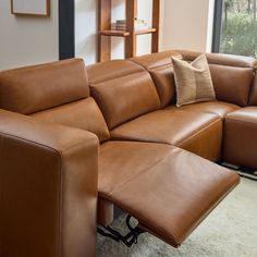 a brown leather sectional sofa with pillows on it's back and arm rests in front of a large window