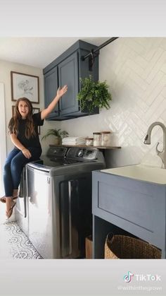 a woman sitting on top of a washing machine in a kitchen next to a sink