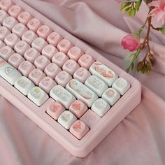 a pink and white computer keyboard sitting on top of a bed next to a flower