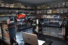 a laptop computer sitting on top of a desk in a room filled with shelves and bins