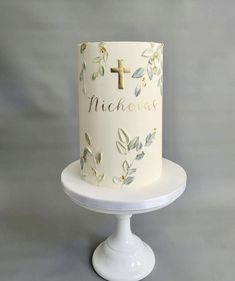 a white cake with gold leaves and a cross on top is sitting on a pedestal