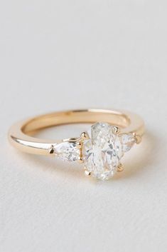 a gold ring with three pear shaped diamonds on the side and an oval diamond in the middle