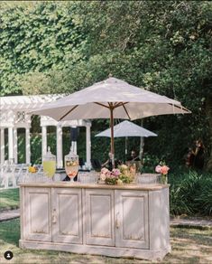 an outdoor bar with umbrellas and flowers on the table in front of some trees