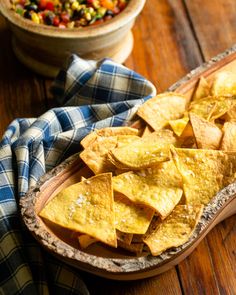 tortilla chips on a wooden platter with a bowl of salsa in the background