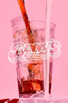 a glass filled with liquid and ice on top of a pink table next to a white sign