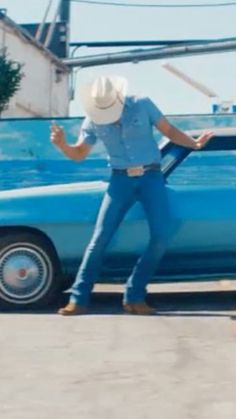 a man standing next to a blue car in front of a building with a white hat on