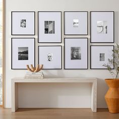 a white table sitting in front of a wall with pictures on it and a potted plant next to it