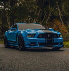 a blue mustang parked on the side of a road with trees in the back ground