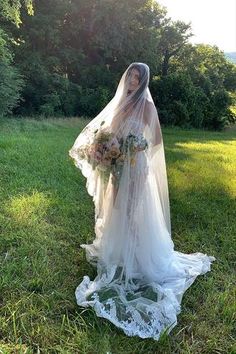 a woman in a wedding dress is standing on the grass with her veil over her head