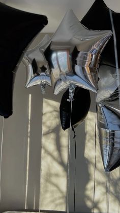 black and silver balloons are hanging from the ceiling in front of a white wall with shadows on it