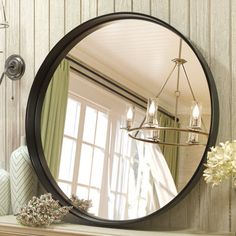 a round mirror sitting on top of a mantle next to a vase with flowers in it