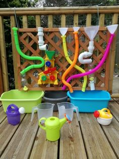 plastic toys are sitting on a wooden deck near watering hoses and buckets with water coming out of them