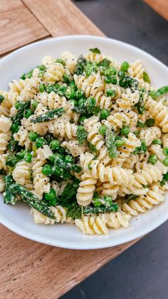 a white bowl filled with pasta and broccoli on top of a wooden table