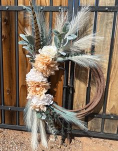 a wreath made out of feathers and flowers on top of a wooden fence next to a metal gate