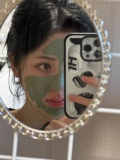 a woman holding up a cell phone in front of her face with a green mask on