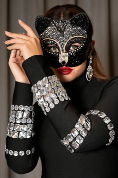 a woman wearing a black mask with silver jewels on her arm and hands in front of her face