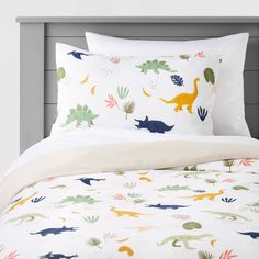 a bed with dinosaurs and plants printed on the pillow cases, along with two pillows