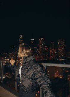 a woman standing on top of a building at night with the city lights in the background