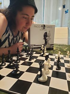 a woman playing chess on a table with an open book in front of her,