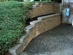 a stone wall with steps leading up to it and green bushes growing on the side