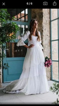 a woman in a white wedding dress standing by a blue door with her hands on her hips